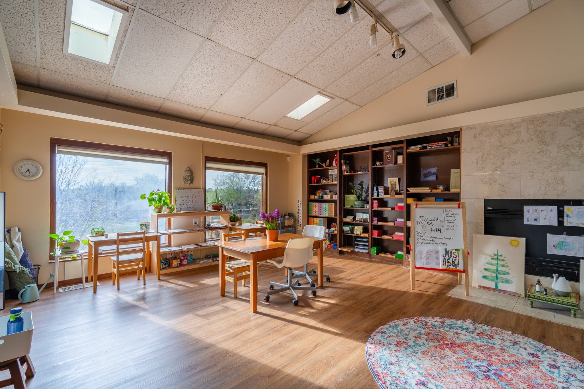 A sunlit classroom with wooden shelves, plants along the windowsill, and child-sized tables