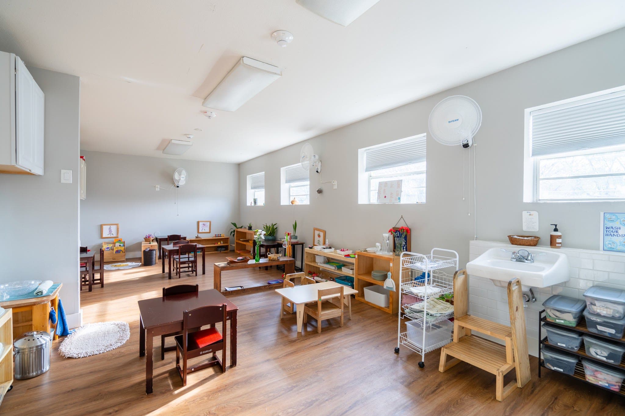A bright, open classroom with prepared materials, a hand-washing station, and natural light