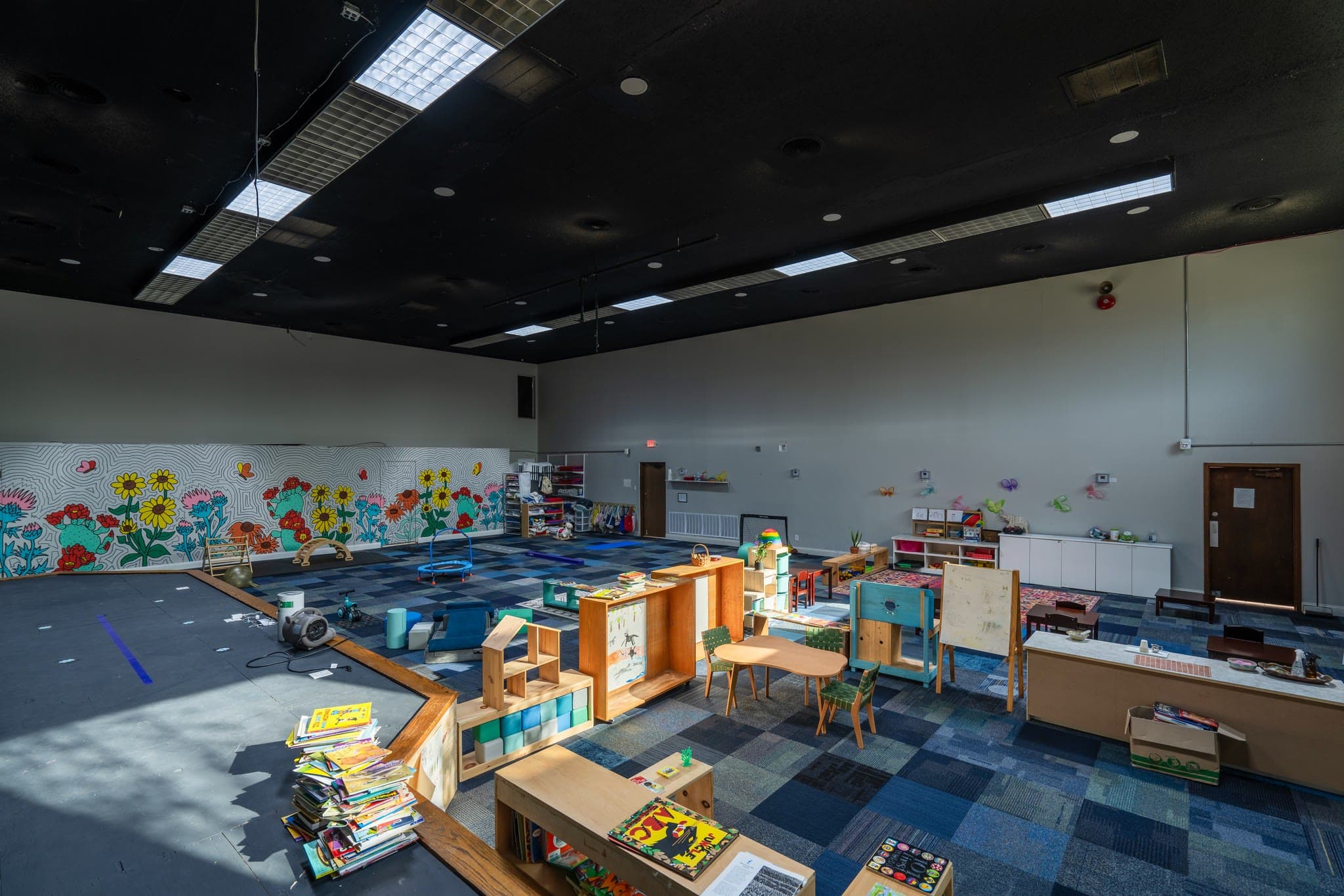 A large community room with a painted mural, soft carpet, and open work spaces